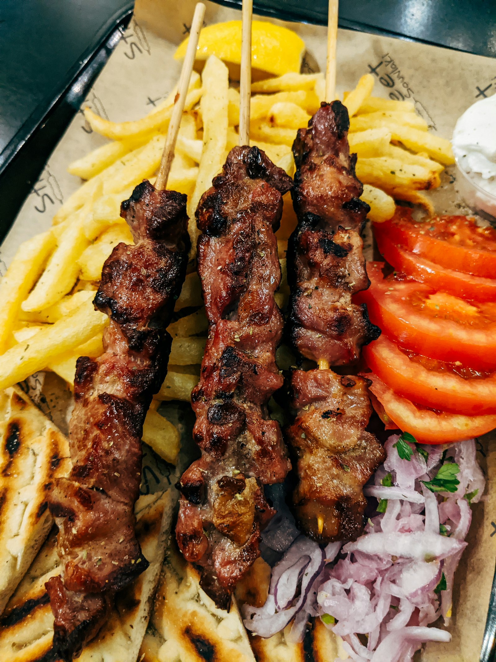 Gegrillte Fleischspieße auf Fladenbrot mit Pommes, Tomaten und Zwiebeln